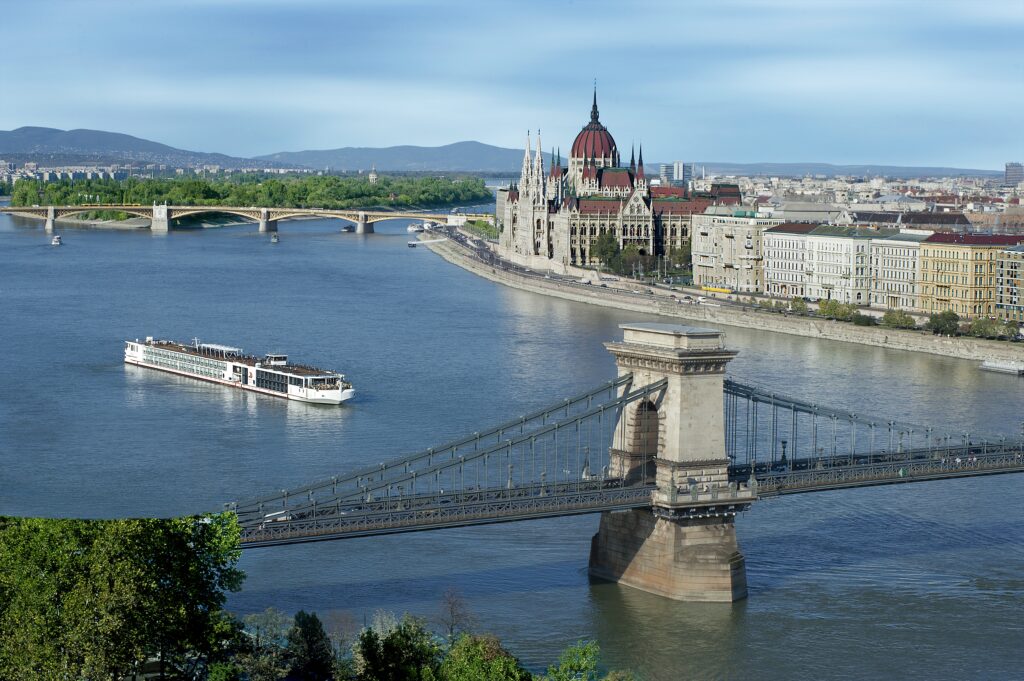 A glatt kosher cruise ship sails along a scenic European river, passing historic landmarks and elegant architecture, offering a luxury kosher cruises experience.